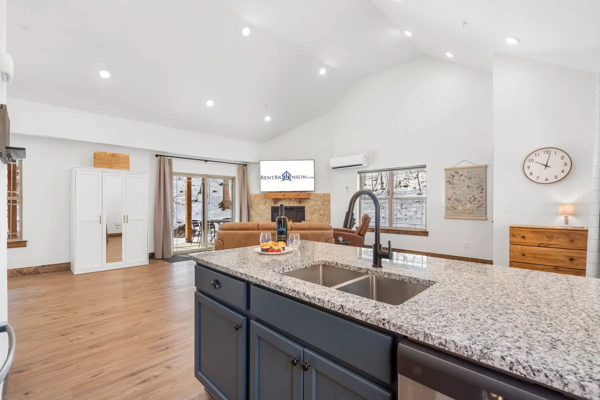 A bright kitchen with a spacious granite-topped island sink, comfortable seating area, and large windows that flood the room with daylight. It feels inviting for both casual breakfasts and intimate dinners.