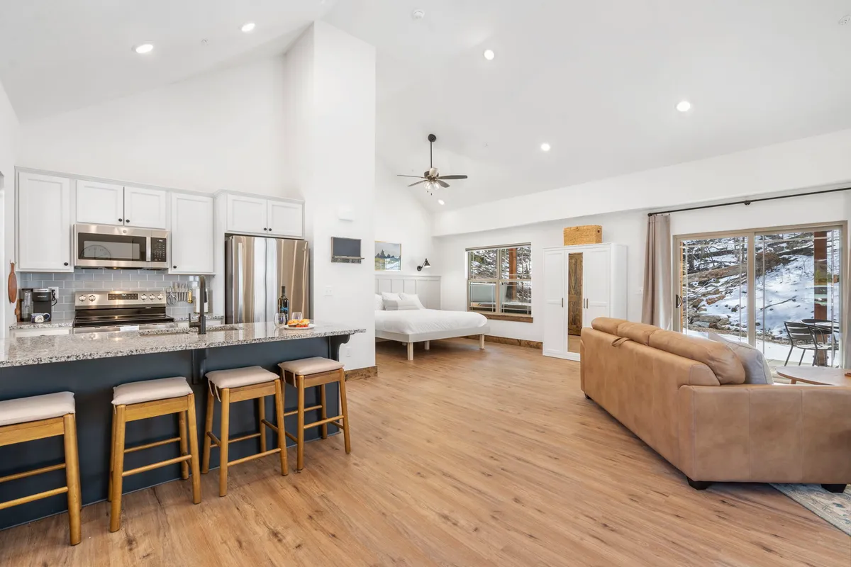 A cozy kitchen and living area with a kitchen island, large windows that bathe the space in sunlight, and a comfortable sofa nearby. The seamless layout encourages socializing while cooking or relaxing.