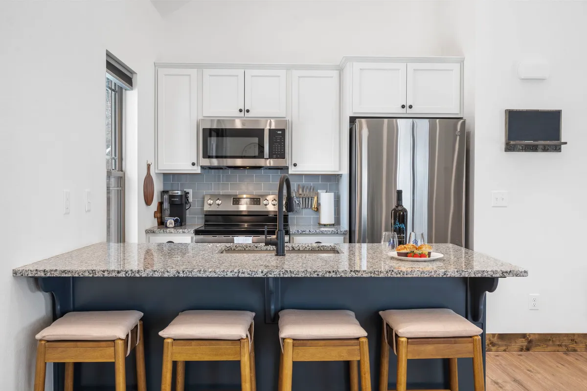 The image showcases the stylish interior of the Everwood Escape cabin's kitchen and dining area, featuring a gleaming granite countertop with bar stools, stainless steel appliances, and a wine bottle with glasses set out—suggesting an inviting space for socializing, casual dining, and making memories together.