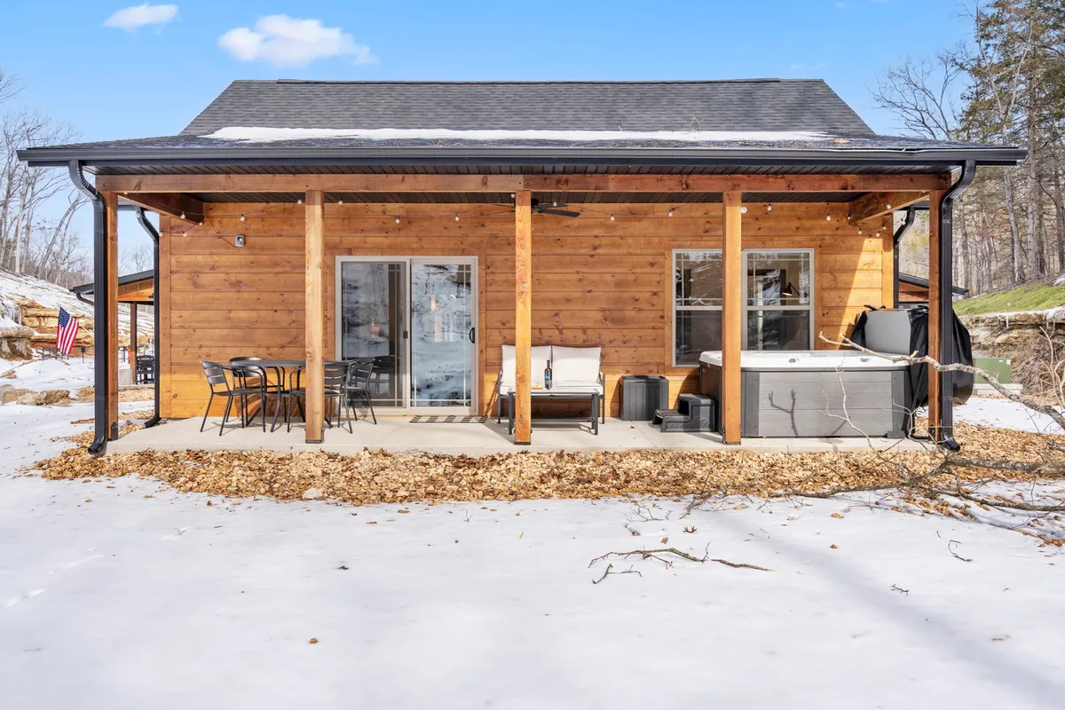 A cozy wooden structure nestled among trees features a private hot tub on the deck, inviting outdoor seating, and a tranquil natural backdrop. The area is surrounded by lush greenery and exudes peaceful seclusion, making it ideal for relaxing and stargazing in privacy.