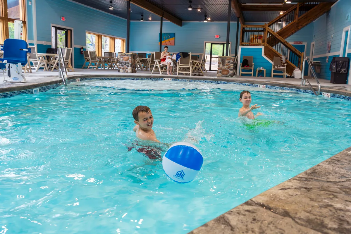 A lively indoor pool scene filled with children playing with beach balls, natural light streaming in through large windows, and comfortable seating areas for parents and families to relax. The atmosphere is playful and energetic, capturing moments of family fun and togetherness.